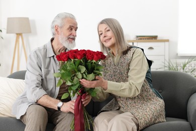 Photo of Happy couple with bouquet of red roses on sofa at home