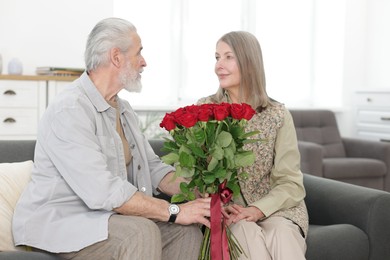 Photo of Lovely couple with bouquet of red roses on sofa at home