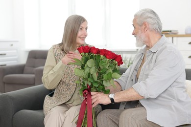 Photo of Happy couple with bouquet of red roses on sofa at home