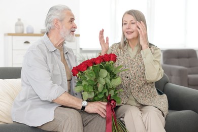 Photo of Happy couple with bouquet of red roses on sofa at home