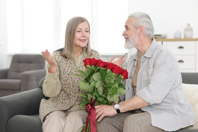 Photo of Happy couple with bouquet of red roses on sofa at home