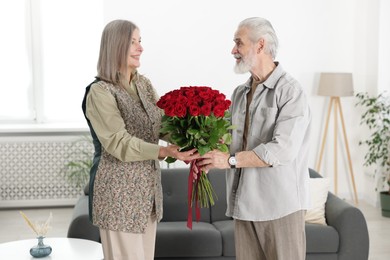 Photo of Happy couple with bouquet of red roses at home