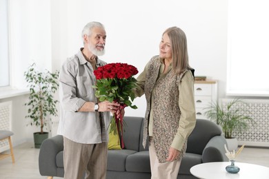 Photo of Happy couple with bouquet of red roses at home