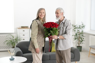 Photo of Happy couple with bouquet of red roses at home