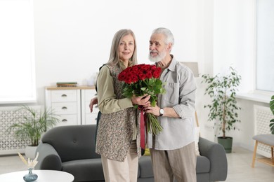 Photo of Happy couple with bouquet of red roses at home