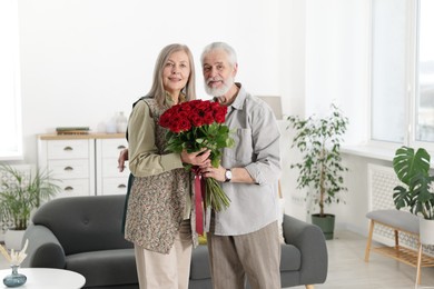 Photo of Happy couple with bouquet of red roses at home