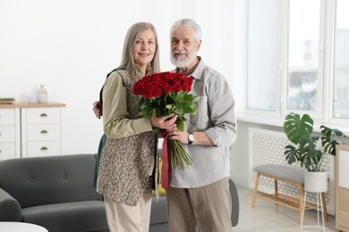 Photo of Happy couple with bouquet of red roses at home