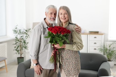 Photo of Happy couple with bouquet of red roses at home