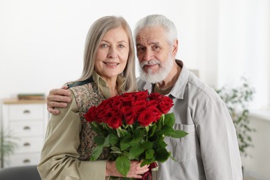 Photo of Happy couple with bouquet of red roses at home