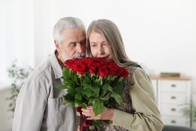 Photo of Cute couple with bouquet of red roses at home