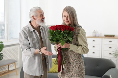 Photo of Happy couple with bouquet of red roses at home