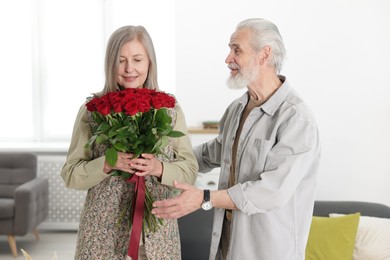 Photo of Happy couple with bouquet of red roses at home