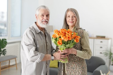 Photo of Cute couple with bouquet of tulips at home