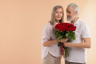 Photo of Cute couple with bouquet of red roses on beige background. Space for text