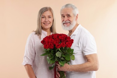 Photo of Happy couple with bouquet of red roses on beige background