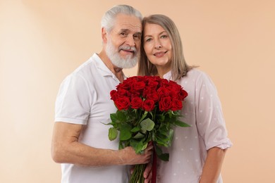 Photo of Happy couple with bouquet of red roses on beige background