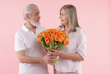 Photo of Happy couple with bouquet of tulips on pink background