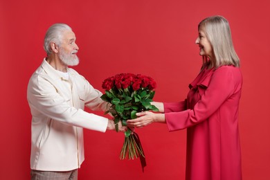 Photo of Man presenting bouquet of roses to his happy wife on red background