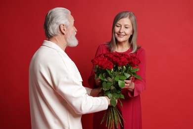 Photo of Man presenting bouquet of roses to his happy wife on red background