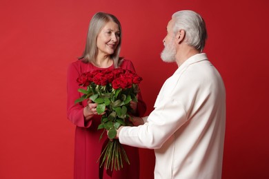 Photo of Man presenting bouquet of roses to his happy wife on red background