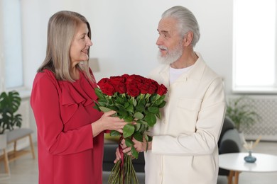 Photo of Happy couple with bouquet of red roses at home