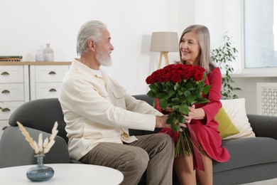 Photo of Happy couple with bouquet of red roses on sofa at home