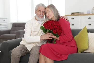 Photo of Happy couple with bouquet of red roses on sofa at home