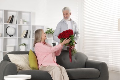 Photo of Man presenting bouquet of roses to his wife at home