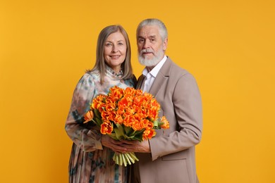 Photo of Happy couple with bouquet of tulips on yellow background