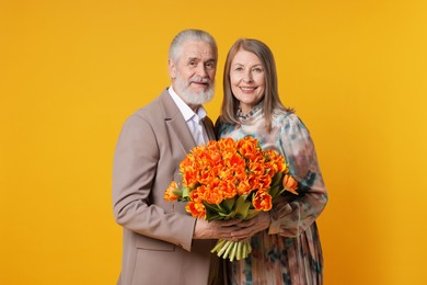 Photo of Happy couple with bouquet of tulips on yellow background