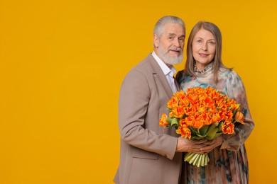 Photo of Cute couple with bouquet of tulips on yellow background. Space for text