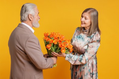 Photo of Man presenting bouquet of tulips to his happy wife on yellow background