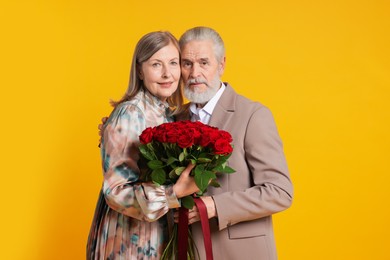 Photo of Happy couple with bouquet of red roses on yellow background