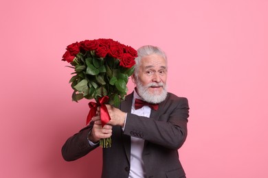 Photo of Senior man with bouquet of red roses on pink background