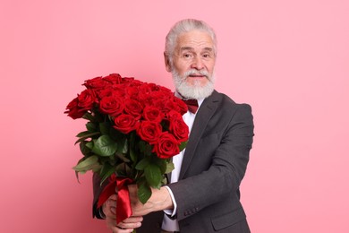 Photo of Senior man with bouquet of red roses on pink background