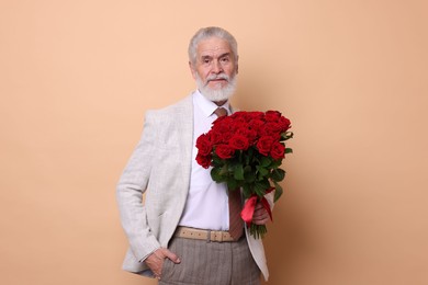 Photo of Senior man with bouquet of red roses on beige background