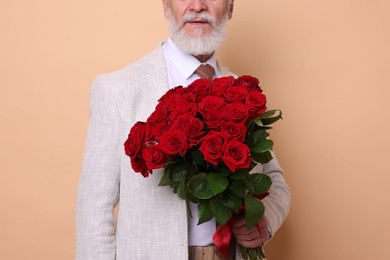 Photo of Senior man with bouquet of red roses on beige background, closeup