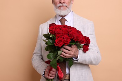 Photo of Senior man with bouquet of red roses on beige background, closeup