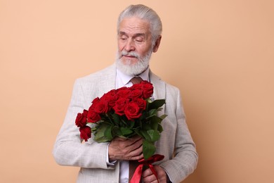 Photo of Senior man with bouquet of red roses on beige background