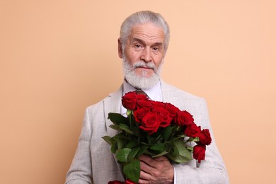 Photo of Senior man with bouquet of red roses on beige background