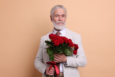 Photo of Senior man with bouquet of red roses on beige background