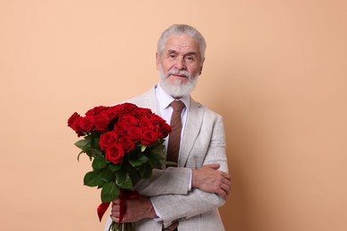 Photo of Senior man with bouquet of red roses on beige background