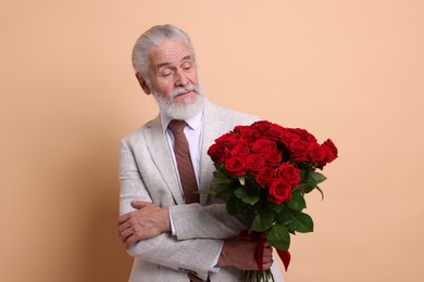 Photo of Senior man with bouquet of red roses on beige background