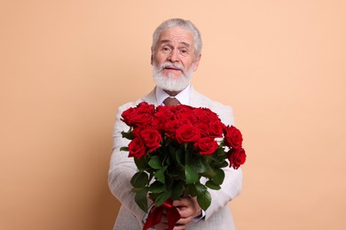 Photo of Senior man with bouquet of red roses on beige background