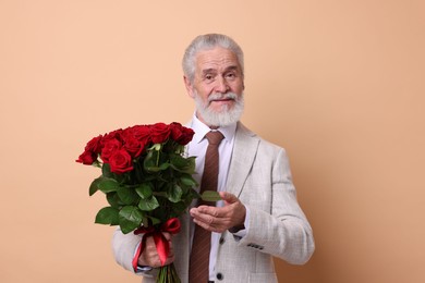 Photo of Senior man with bouquet of red roses on beige background