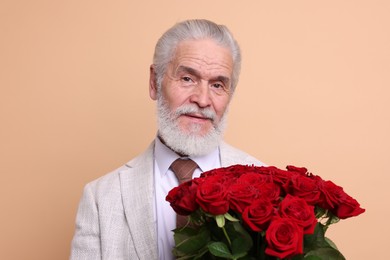 Photo of Senior man with bouquet of red roses on beige background