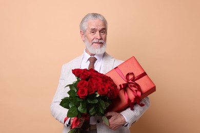 Photo of Senior man with bouquet of red roses and gift box on beige background