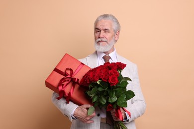 Photo of Senior man with bouquet of red roses and gift box on beige background