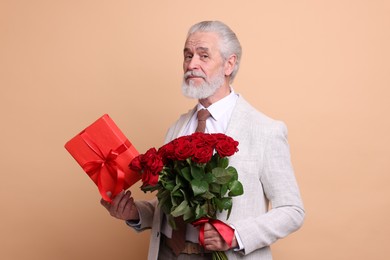 Photo of Senior man with bouquet of red roses and gift box on beige background