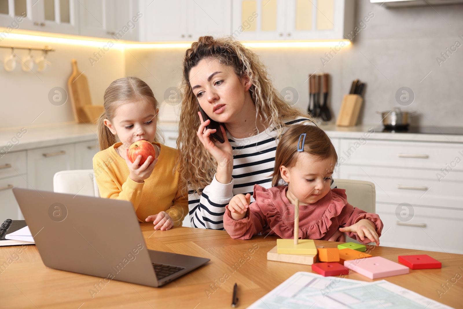 Photo of Single mother talking on smartphone and her daughters at table in kitchen